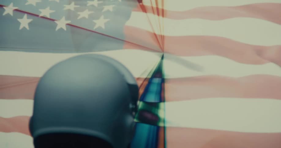 A person in a white helmet faces a large american flag viewed from behind