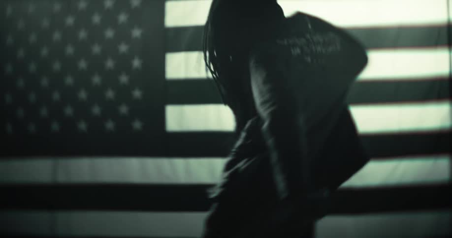 A black man with long braids is dancing in front of a large american flag