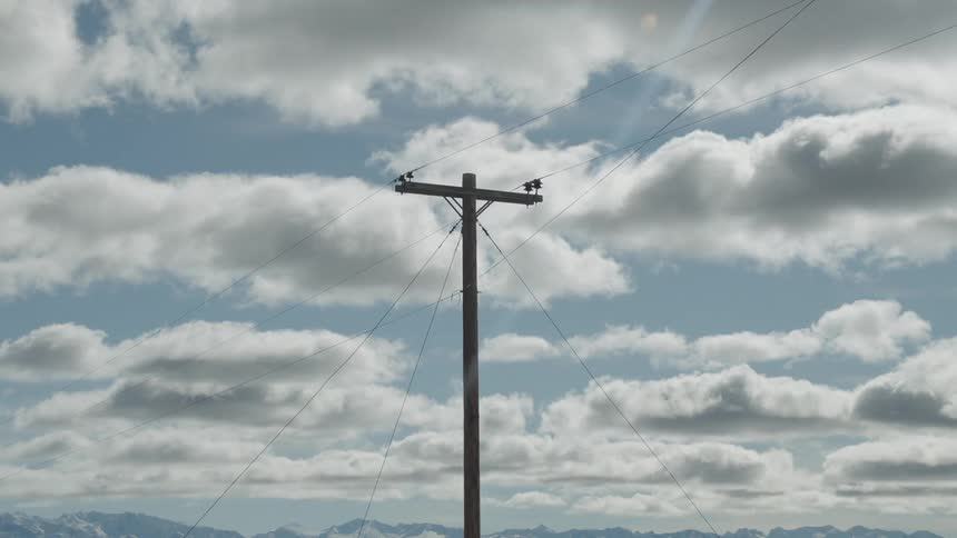 Utility pole standing alone against a backdrop of a partly cloudy sky with electrical wires extending diagonally outward in various directions