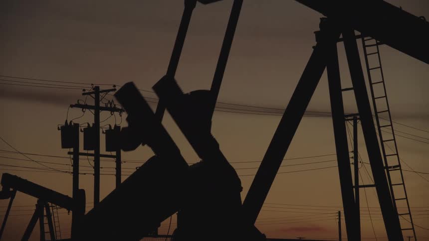 An oil rig machine continuously drilling crude oil from the ground at sunset