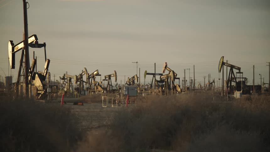 Several oil extraction pumps operate in an arid field at dusk