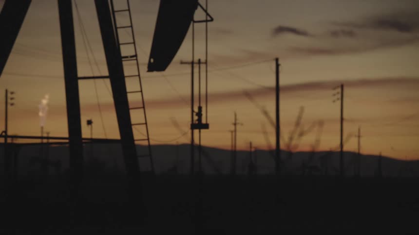 An oil rig machine continuously drilling crude oil from the ground at sunset