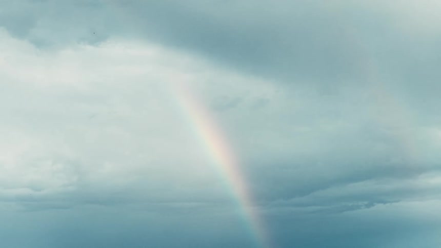 Rainbow cutting diagonally through a cloudy sky
