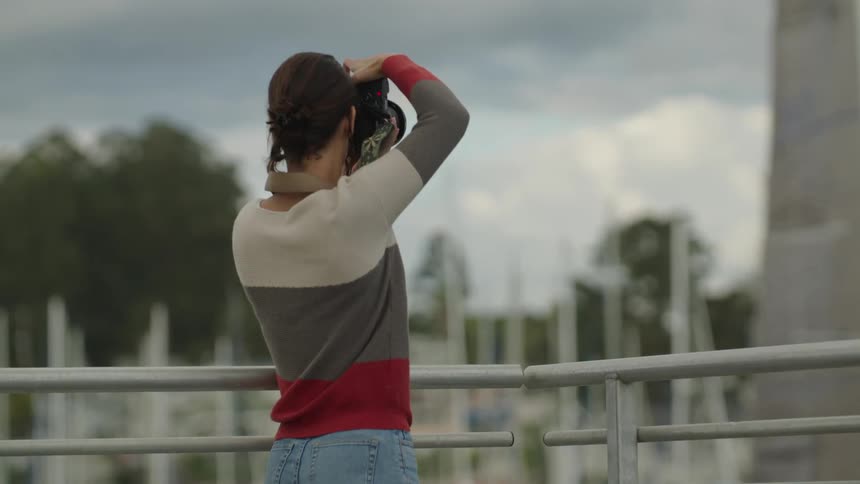 Person holding a digital camera taking a photograph behind a metal railing
