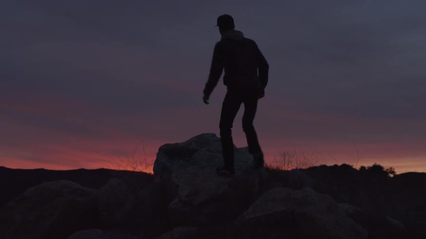 Man climbing on top of a rock on a trail at dawn