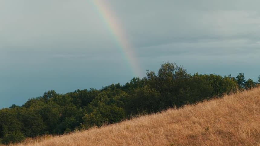 Landscape of a hill with a rainbow in the background on a cloudy day