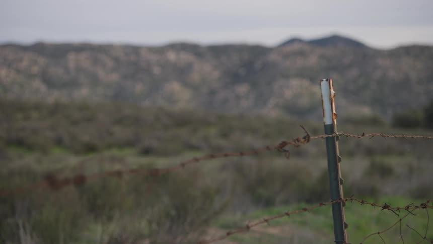 Barbed wire fence in the foreground with a field and mountains in the background