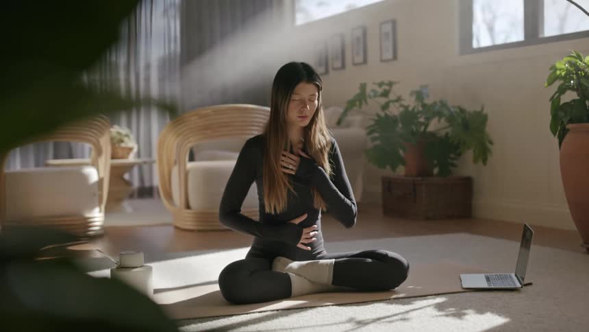 Woman sitting crosslegged with eyes closed relaxing on a living room rug