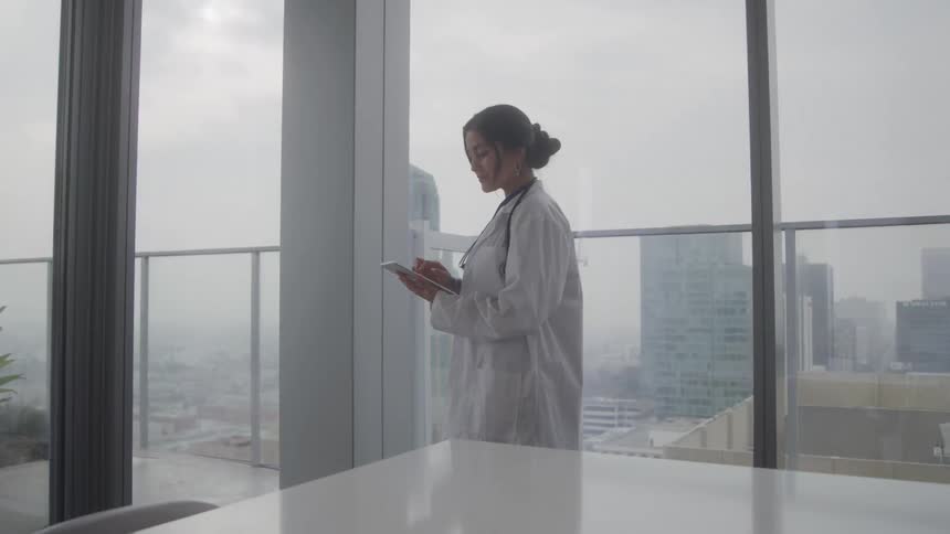 A woman stands in the corner of a room on her tablet