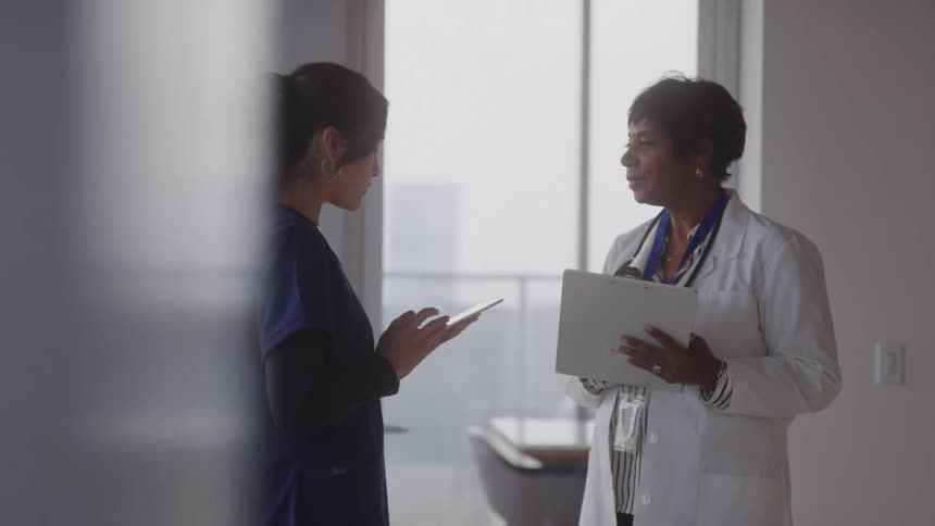 Two female medical professionals stand in the hallway having a discussion