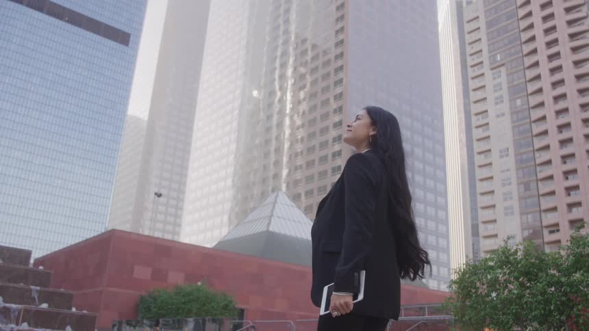 Woman in black blazer walking outdoors in a metropolis with tall buildings