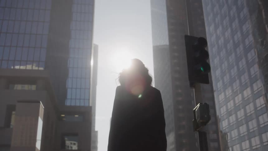 The woman is walking past the tall buildings