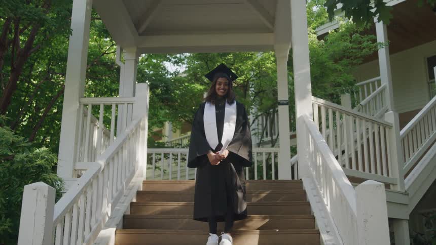 Woman in a stairwell with a happy expression and a graduation gown
