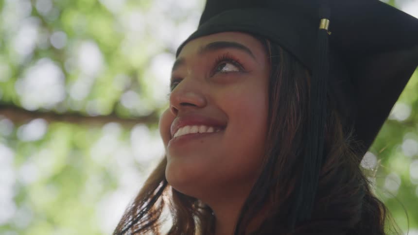 Closeup lowangle shot of a young womans face likely a graduate as she looks upwards with a bright joyful smile