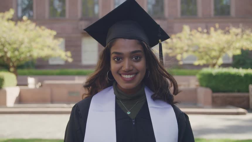 Proud graduate smiles as she stands in front of a large school building