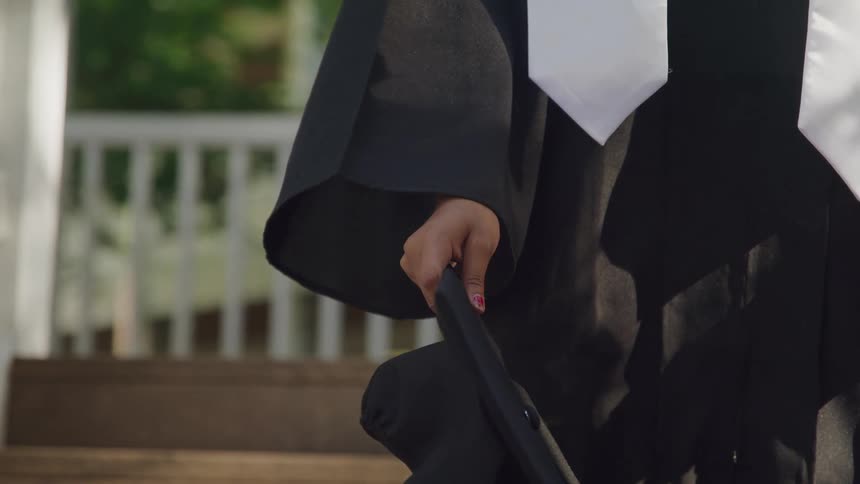 A person in a graduation gown and stole holds a cap then raises it in celebration with a joyful expression and finally throws it into the air