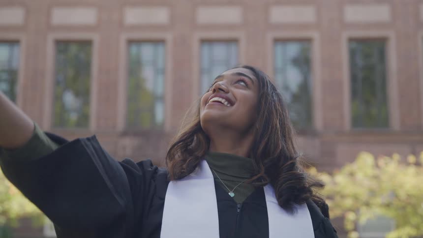 Smiling woman with graduation gown throwing her hat up