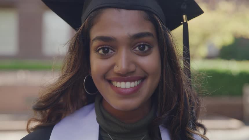 The graduate is smiling while wearing a cap and gown
