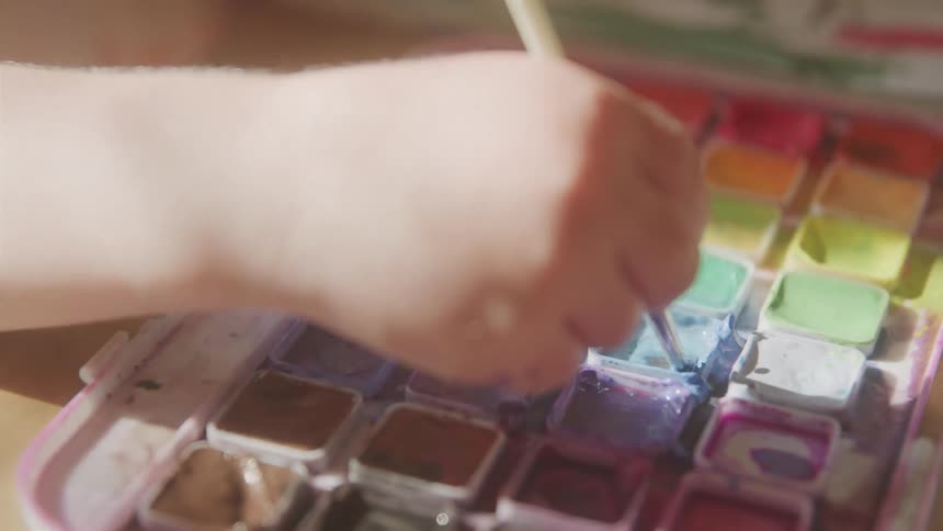 Childs hand holding a paintbrush in a bow of paints