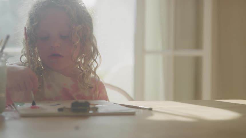 Young girl paints shapes on paper held steady by a clipboard on the table