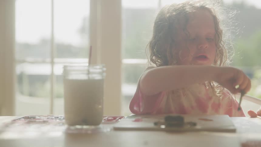 Little girl sitting at a table playing paint with a brush