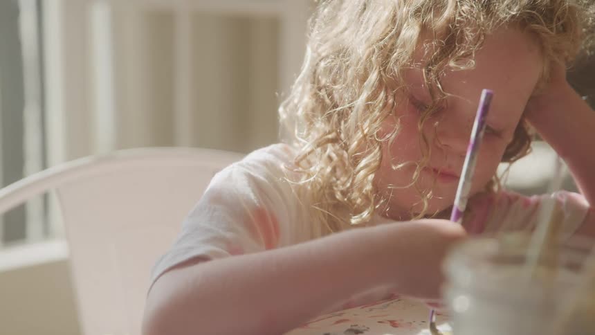 Little blonde girl sitting and drawing with a paintbrush
