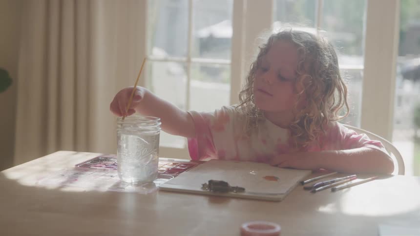 Small girl painting on paper clipped onto a clipboard at a table