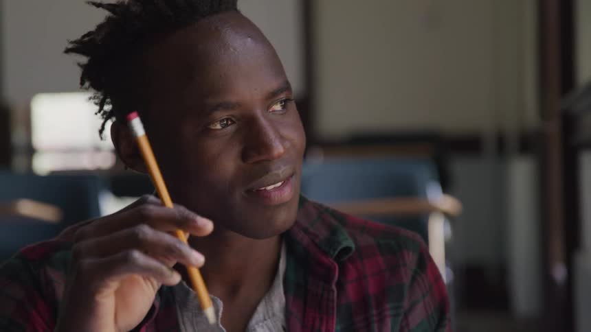 Closeup shot of a young man with dark skin and short textured hair holding a yellow pencil with a pink eraser near his temple