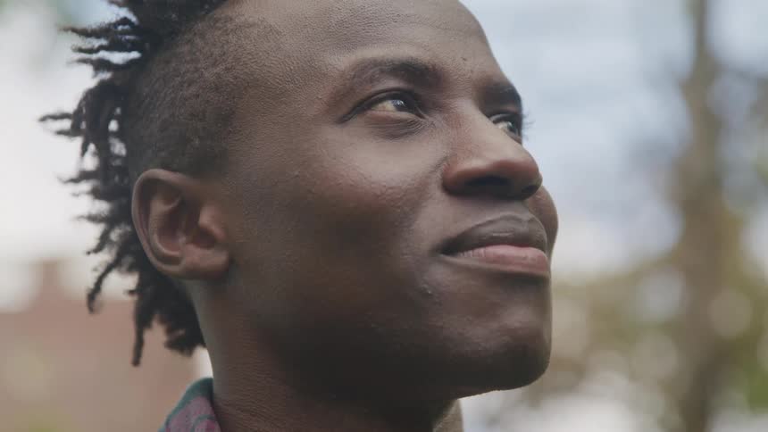 The video features a closeup of a person with dreadlocks looking upward and slightly to the right with a contemplative or hopeful expression the background is blurred suggesting an outdoor setting with natural light