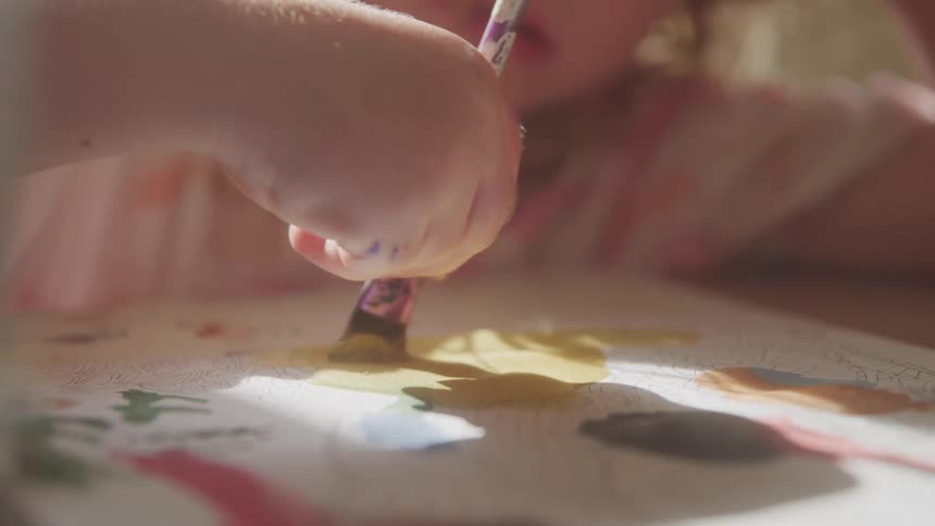 Child leans on an arm while painting with a paintbrush