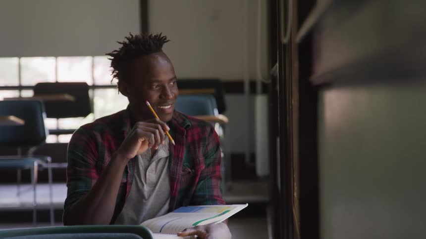 The video features a man with dreadlocks smiling and looking towards the upper right of the frame with a bright natural light illuminating his face the background is softly blurred showing hints of green foliage and a clear sky suggesting an outdoor