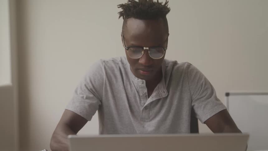Man with glasses sitting at a table and opening laptop