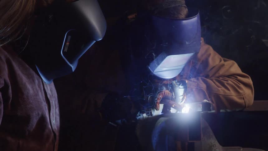 Two people with protective helmets welding an object and sparks coming out