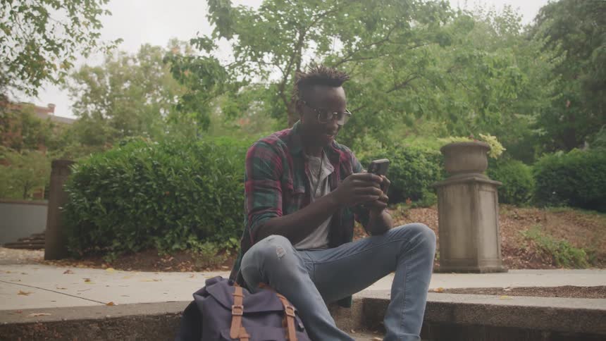 Man sitting in a square with a happy expression and typing on a smartphone