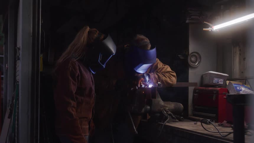 Two people wearing protective masks in a workshop welding an object
