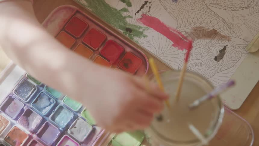 The child dips their brush in the jar of water