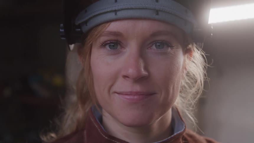 Woman wearing her welding mask pushed up faces forward and smiles