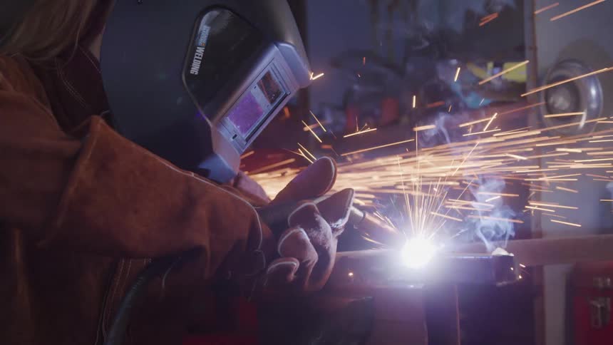 The video features a welder in a dark environment wearing a protective helmet and gloves actively joining metal with a bright arc and accompanying sparks the focused action suggests a skilled industrial task