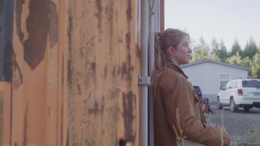 Blonde woman leaning against a rusty container outdoors