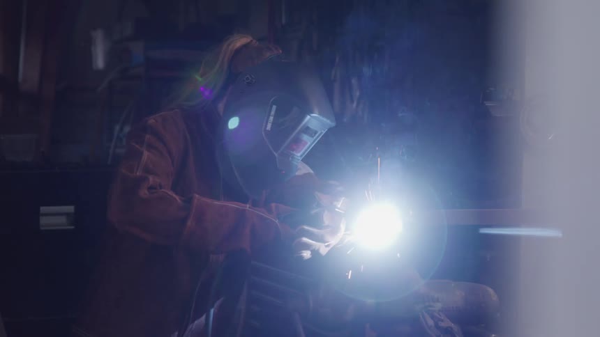 Woman with protective mask performing welding and sparks coming out