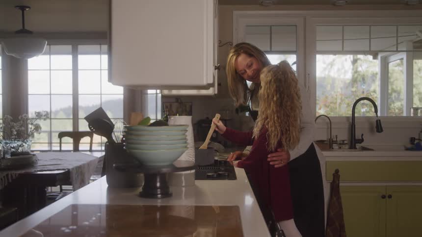 Mother hugging her daughter in the kitchen cooking