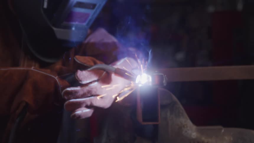 The welder closes her mask and uses a torch