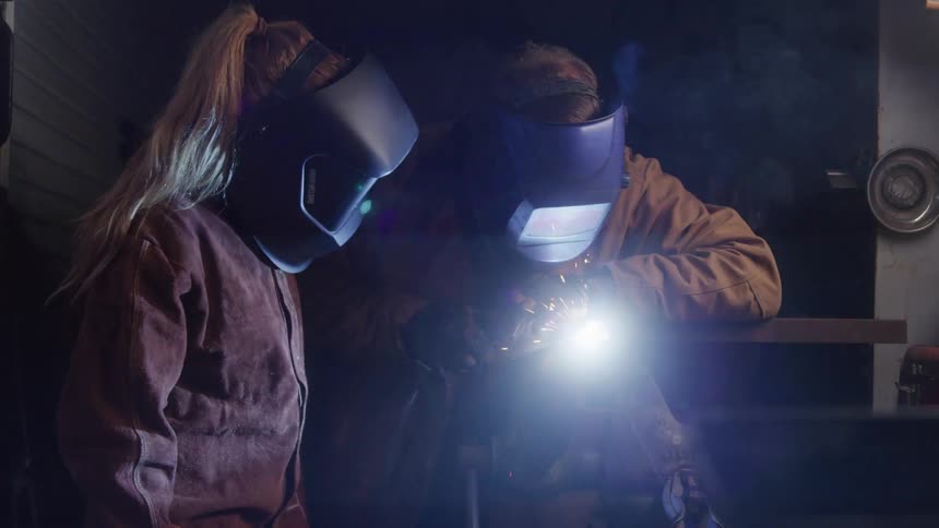Man and a woman both wearing helmets interacting with a welding tool