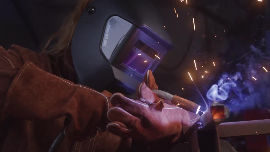 A welder in protective gear fuses metal with a torch as sparks fly in a workshop