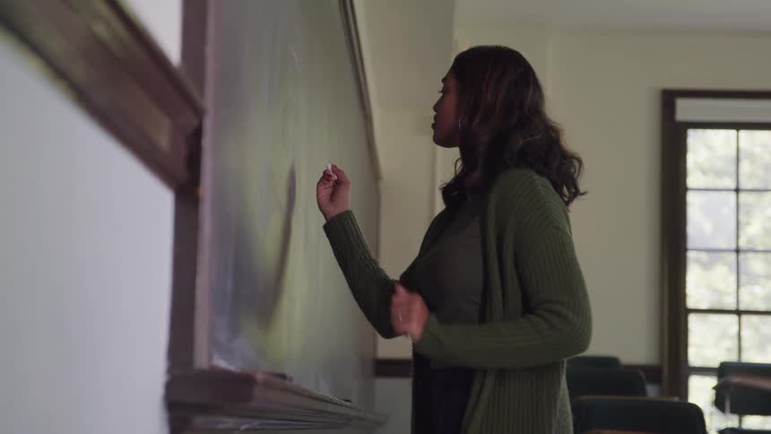 Woman writing on a board with chalk in a classroom