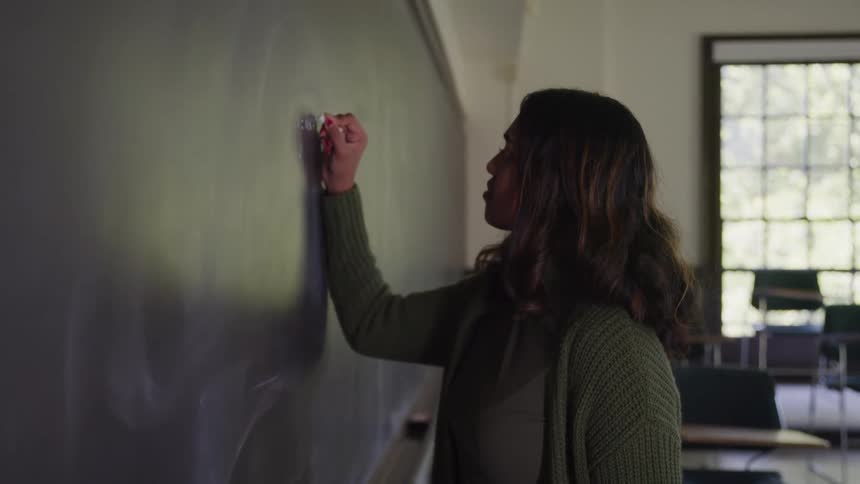 Female teacher writing assignment on the chalkboard in her classroom