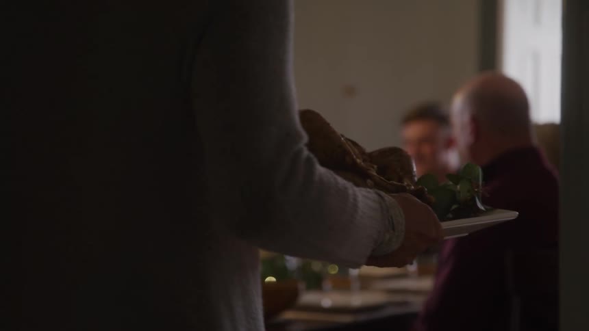 Woman brings a turkey to the table for her already waiting family to enjoy a holiday meal together