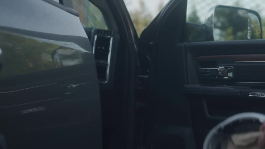 The video shows a closeup of a persons hand reaching out to open the door of a car with a clear focus on the cars handle and mirror the exterior of the car appears to be a dark color possibly gray or black with reflections visible on its polished s
