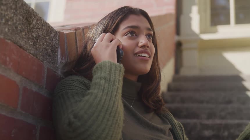 Woman smiles as she sits in a stairway and talks on her phone