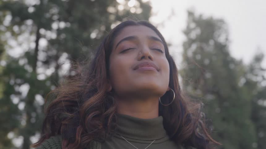 Woman slightly smiles with her eyes closed while enjoying the breeze in the forest